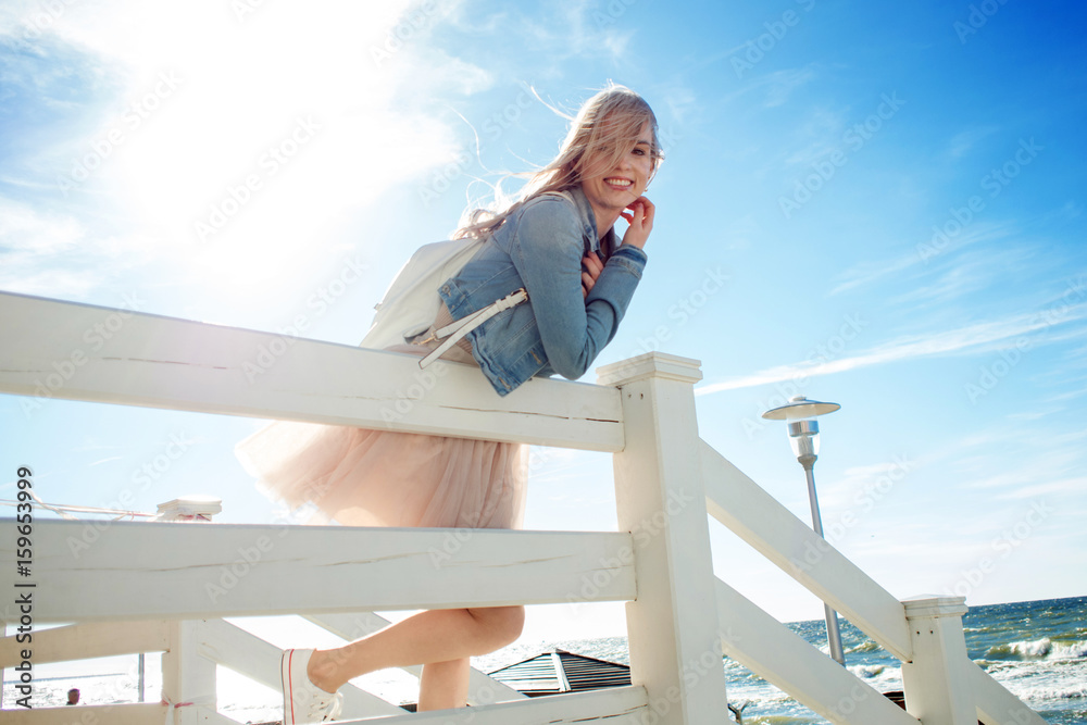 Young cheerful girl on the seashore. Young blonde woman smiling. Trendy beige skirt Young cheerful girl on the seashore. Young blonde woman smiling. Trendy beige skirt