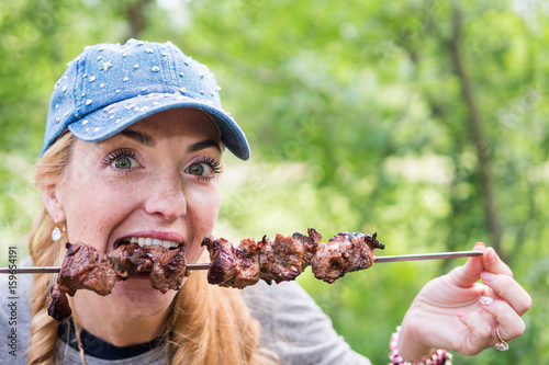 Beautiful freckled woman eating shish kebab, close-up