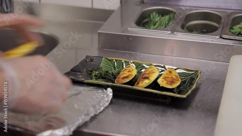 Chef serving traditional Japanese dish served on black stone plate. Baked Mussels with sea kale on course. Close up shooting of hands man in gloves for protection from microbes on workplace in kitchen photo