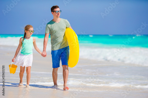 Photography Little girl with beach toys walking along the sea with father