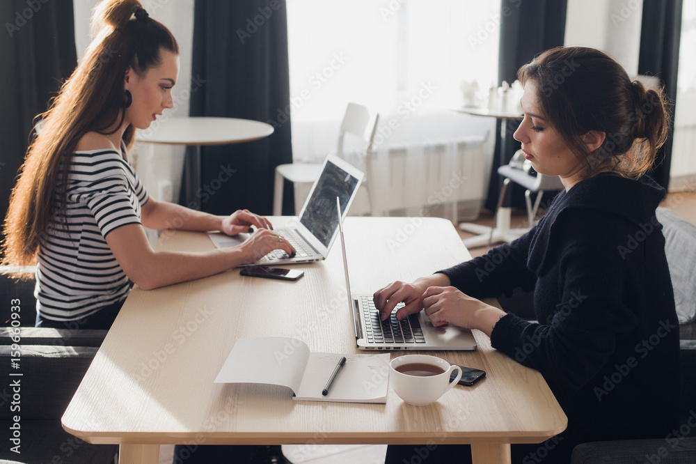 One-on-one meeting. Two young business women sitting at table in cafe. Girl using smartphone. Teamwork, business meeting. Freelancers working. One-on-one meeting. Two young business women sitting at table in cafe. Girl using smartphone. Teamwork, business meeting. Freelancers working.