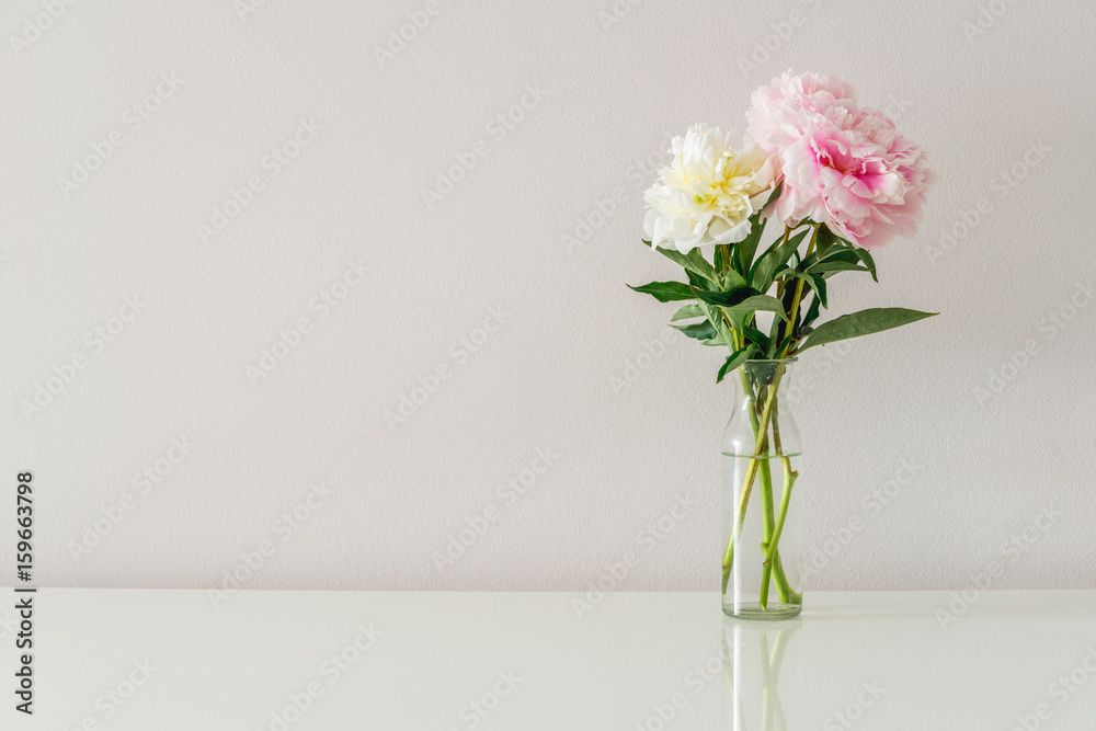 Bouquet of white and pink peonies in glass vase on white background