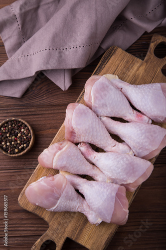 Chicken drumstick on a wooden brown board standing on a wooden background, a jar of peppers, a brown napkin. The process of cooking. Healthy food
