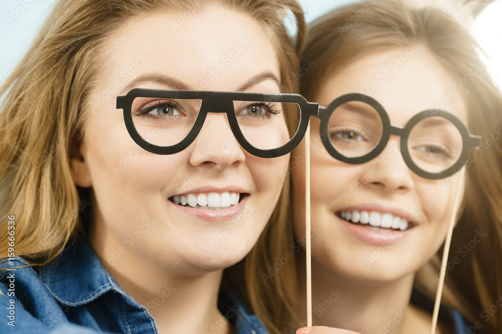 Two happy women holding fake eyeglasses on stick Two happy women holding fake eyeglasses on stick