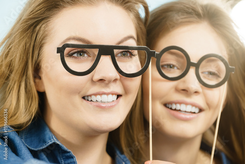 Two happy women holding fake eyeglasses on stick