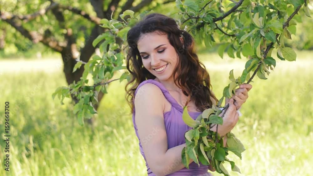 Portrait of a beautiful girl with bright make-up. Caucasian brunette woman posing and looking at camera in lilac or purple dress in the garden. Portrait of a beautiful girl with bright make-up. Caucasian brunette woman posing and looking at camera in lilac or purple dress in the garden.