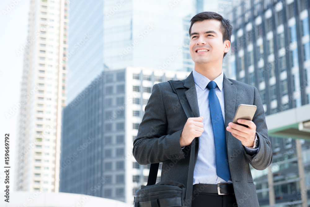 Smiling businessman using mobile phone while carrying bag and walking in the city Smiling businessman using mobile phone while carrying bag and walking in the city
