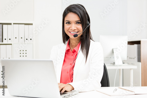 Cuadro en lienzo Businesswoman wearing microphone headset using laptop computer in the office