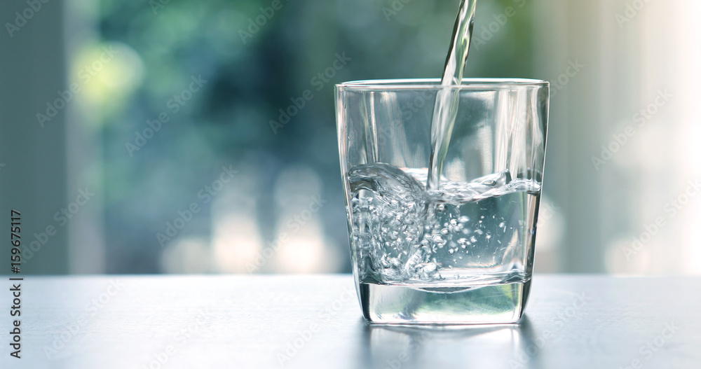 Fototapeta Zamknij się wylewanie oczyszczonej wody świeżego napoju z butelki na stole w salonie