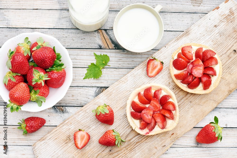 Homemade strawberry tarts on wooden board, cup of milk and bowl of fresh strawberry on wooden table. Countryside summer breakfast concept. Homemade strawberry tarts on wooden board, cup of milk and bowl of fresh strawberry on wooden table. Countryside summer breakfast concept.
