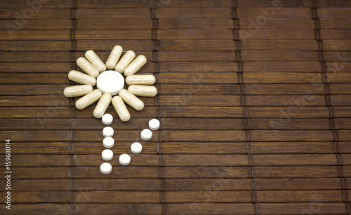 Flower of pills and capsules on a dark wooden background
