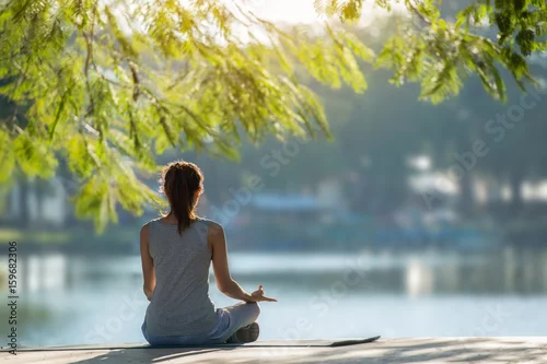 Fototapeta na wymiar Beautiful woman practicing yoga waterfront in the park.