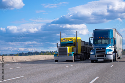 Classic yellow and blue modern semi trucks side by side on the road photo
