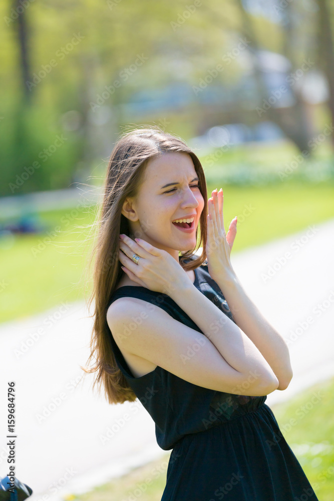 A girl in a summer park is surprised and laughs covering her mouth with her palm A girl in a summer park is surprised and laughs covering her mouth with her palm