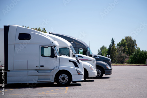 Modern semi trucks stand in row on truck stop parking space