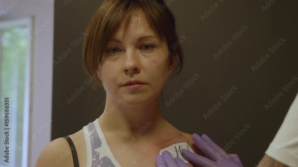 Sleepy female client stands still while tattoo artist glues tattoo design under collarbone Sleepy female client stands still while tattoo artist glues tattoo design under collarbone