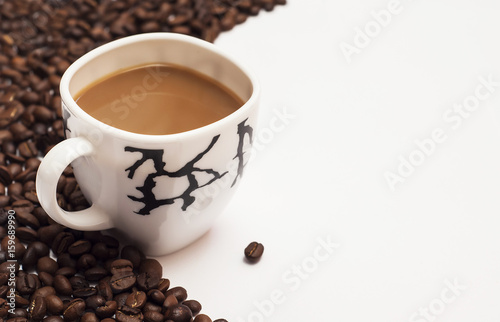 Cup of coffee surrounded by coffee beans on white background
