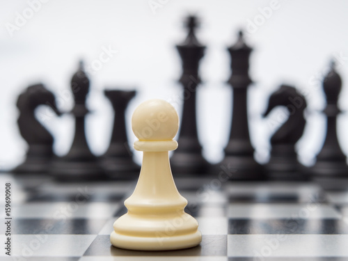 White pawn against the background of dark chess pieces