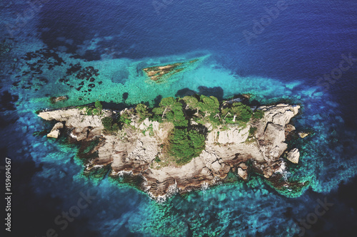 Top view of a rocky island with green trees in the sea