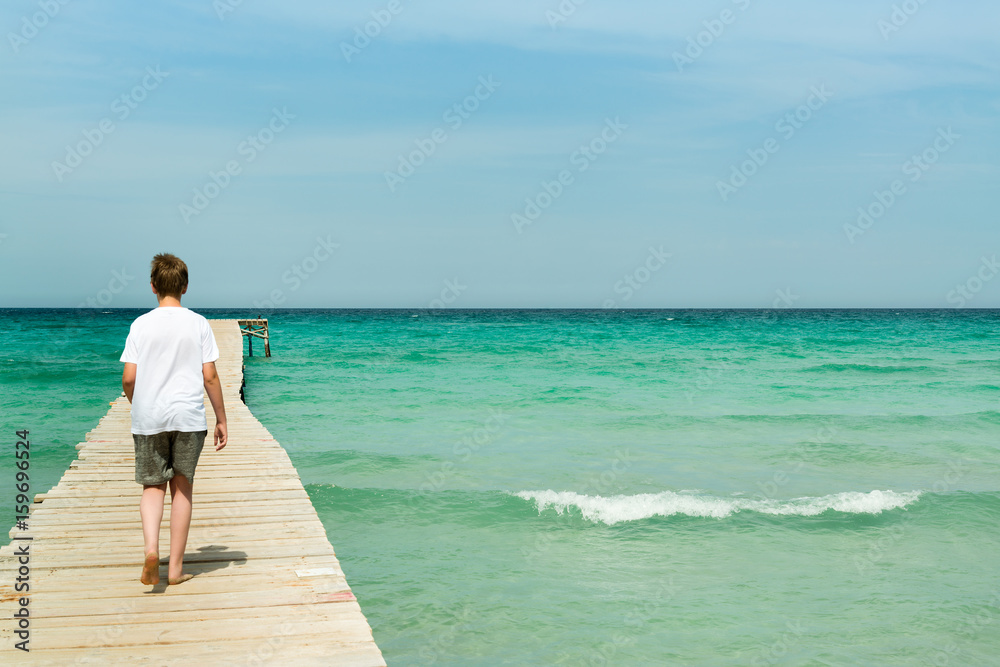 Young man walking on a long wood pier