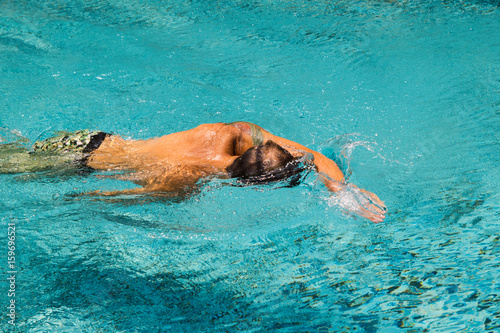 Young man is swimming in a transparent water of a pool in a sunny day.