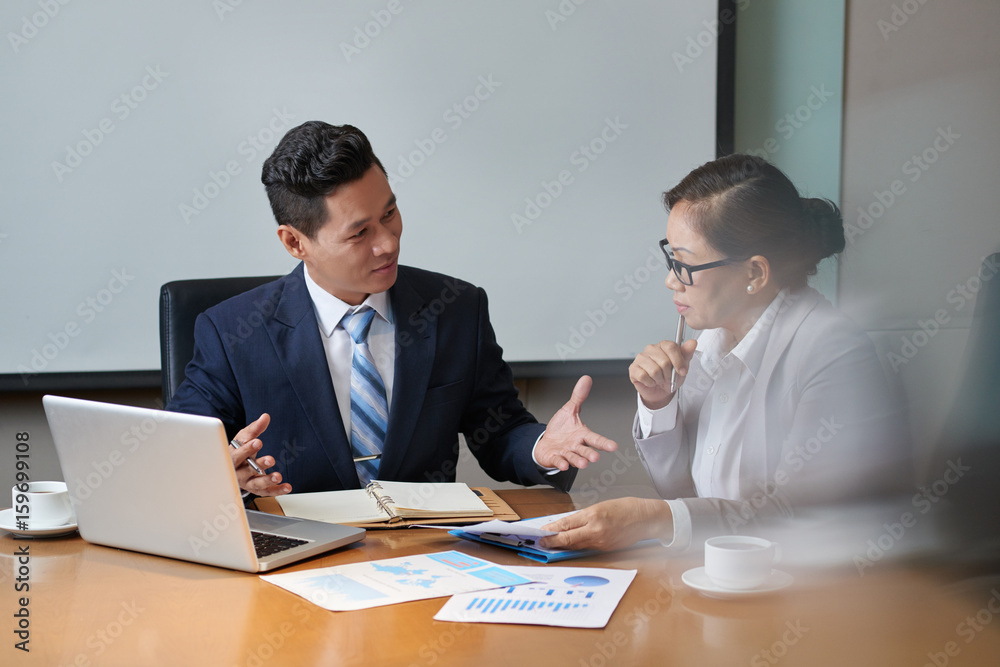 Handsome middle-aged businessman sharing ideas with his female colleague while having meeting in modern boardroom, she listening to him with interest Handsome middle-aged businessman sharing ideas with his female colleague while having meeting in modern boardroom, she listening to him with interest