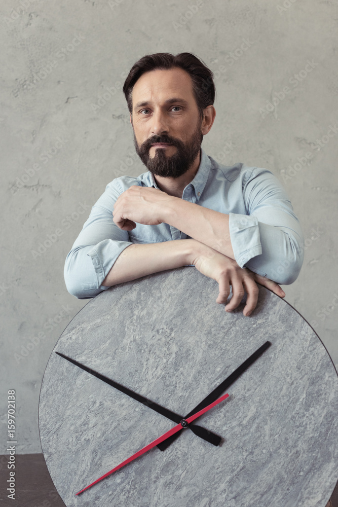pensive bearded man leaning on clock and looking at camera pensive bearded man leaning on clock and looking at camera