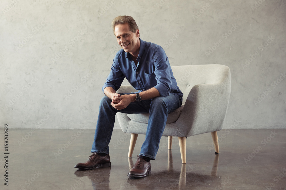 casual middle aged man smiling while sitting on armchair indoors casual middle aged man smiling while sitting on armchair indoors