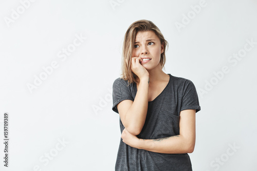 Nervous young pretty girl looking in side biting nails over white background.