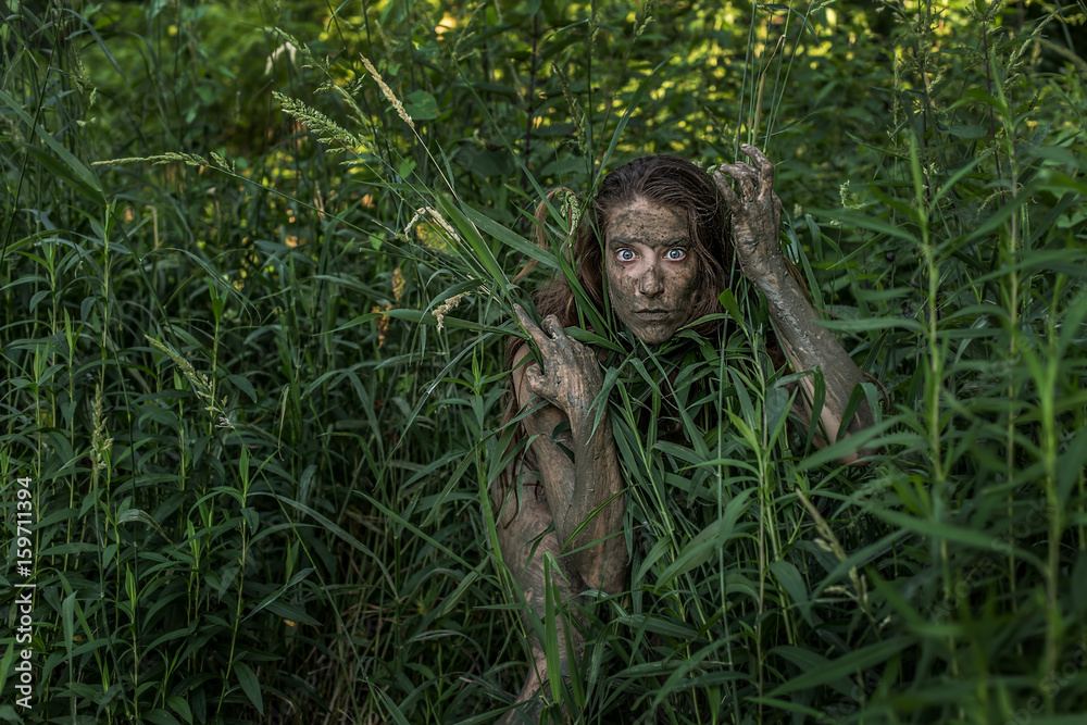 Muddy Amazon brown-haired girl hiding behind a bush in the woods
