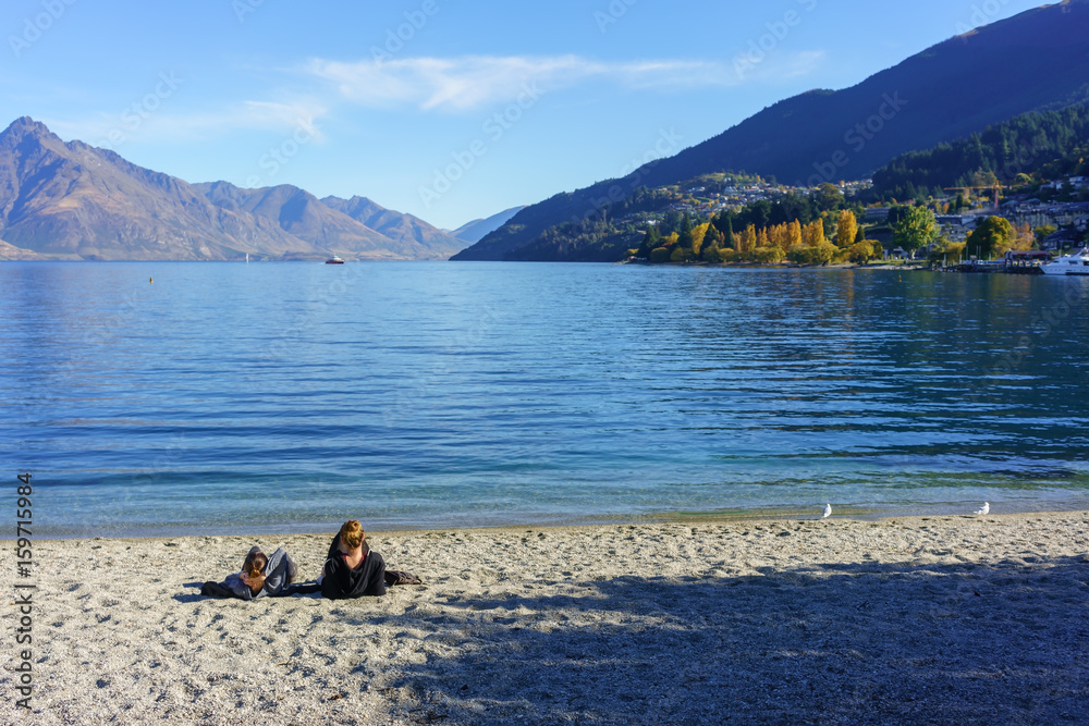 Two young women relaxing on the beach of Lake Wakatipu , Queenstown , South Island of New Zealand Two young women relaxing on the beach of Lake Wakatipu , Queenstown , South Island of New Zealand