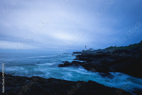 A lighthouse shines through dark clouds along the coast, Portland, Maine