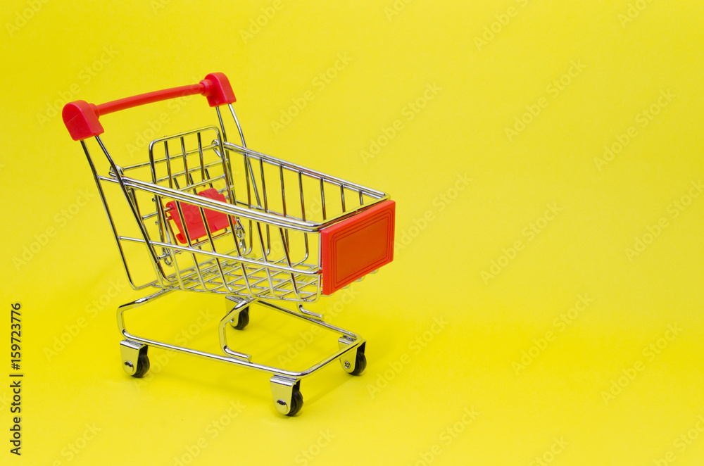 mini red color supermarket shopping cart on yellow background, holiday sale and online shopping concept, selective focus, copy space