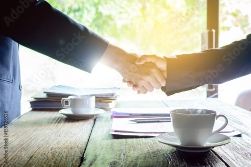 coffee mug on a wooden desk and a businessman shaking hands