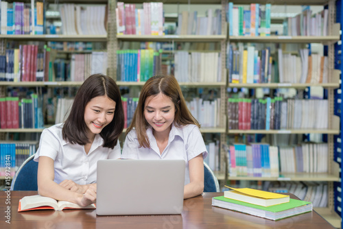 Asian happy students with laptop computer working and studying in library. People, education, technology and school concept