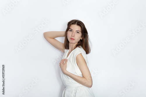 Young beautiful brunette beginner model woman in white blouse practicing posing showing emotions on white wall studio background