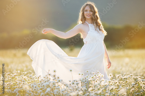 Beautiful happy pregnant girl on the field of daisy flowers, sunset time