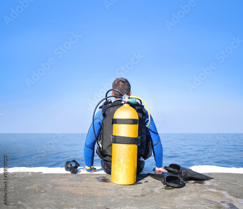 Scuba diver sit on a pier, looking the sea