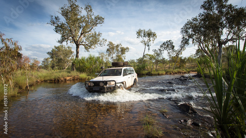 A Four wheel drive vehicle crosses a flowing creek in the far North Kimberley of Western Australia on the road to Mitchell Plateau.