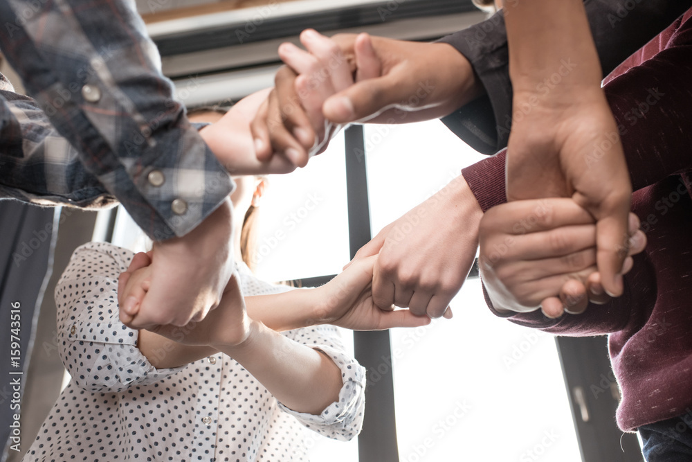 Close-up partial view of teenagers holding hands together indoors, teenagers having fun concept