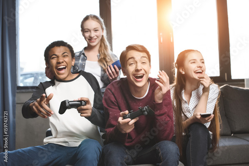 happy multicultural teenagers playing video games with joysticks at home, teenagers having fun concept © LIGHTFIELD STUDIOS