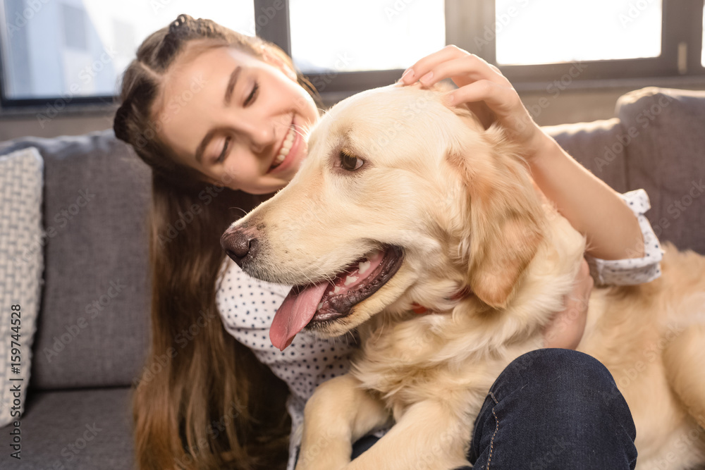 teenager girl hugging golden retriever dog on sofa at home