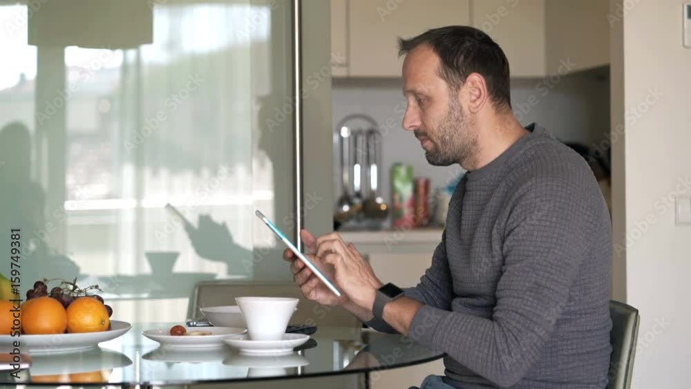 Young man using tablet computer sitting by tablet in kitchen at home
Young man using tablet computer sitting by tablet in kitchen at home