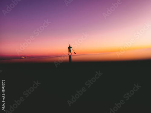 Stand up paddle surfing in ocean with beautiful colorful sunset or sunrise colors