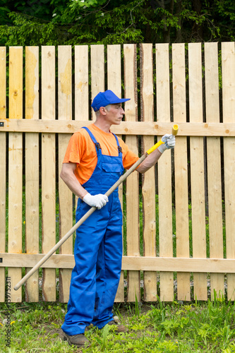 Handyman in blue working uniform checks the condition of paint roller in garden