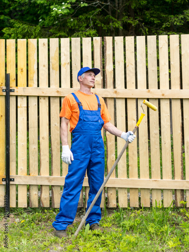 Handyman in blue overalls dreaming on the rest with paint roller in hand