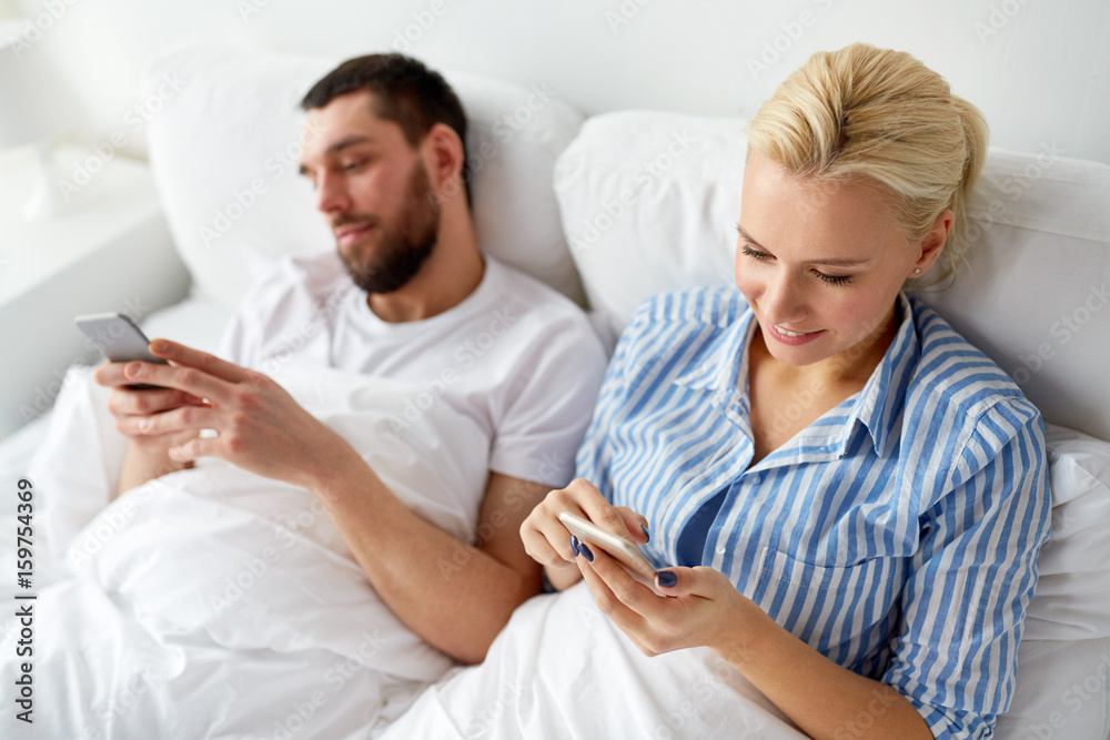 Obraz premium couple with smartphones in bed at home