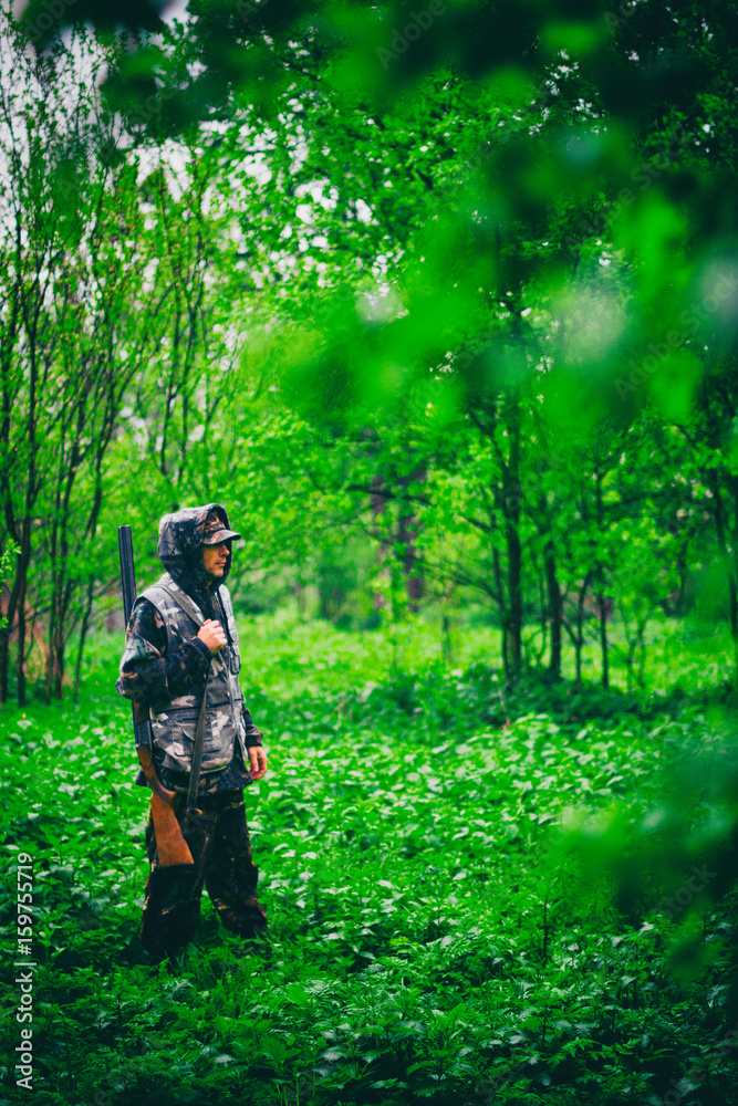Male hunter with a gun walks in rainy weather in the spring forest, tinted photo