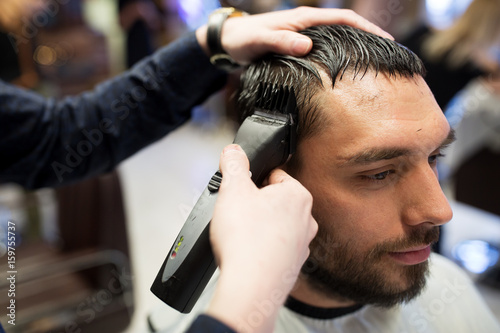 man and barber hands with trimmer cutting hair