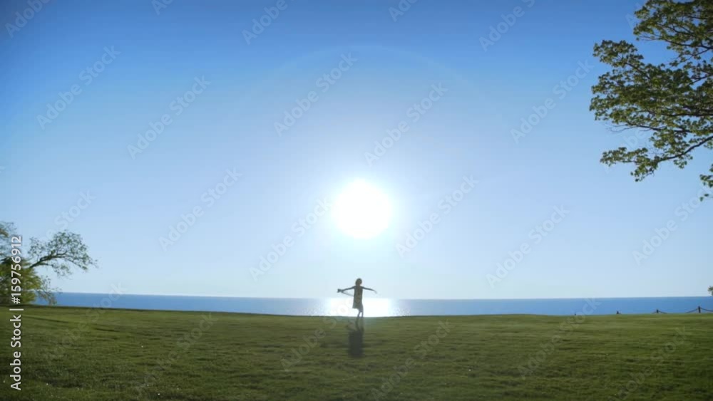 Young beautiful Woman in black dress with black transparent cloth is dancing on the sea at sunrise.